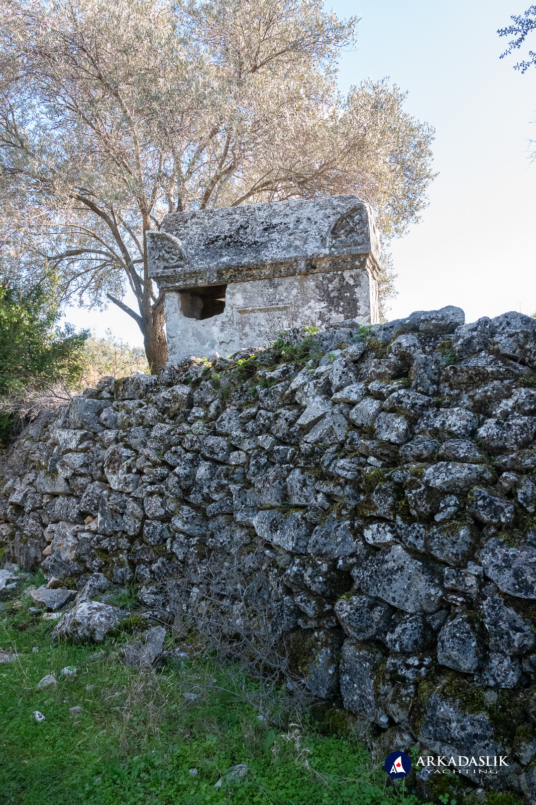 Tall monumental tomb rising above a stone wall at Sidyma