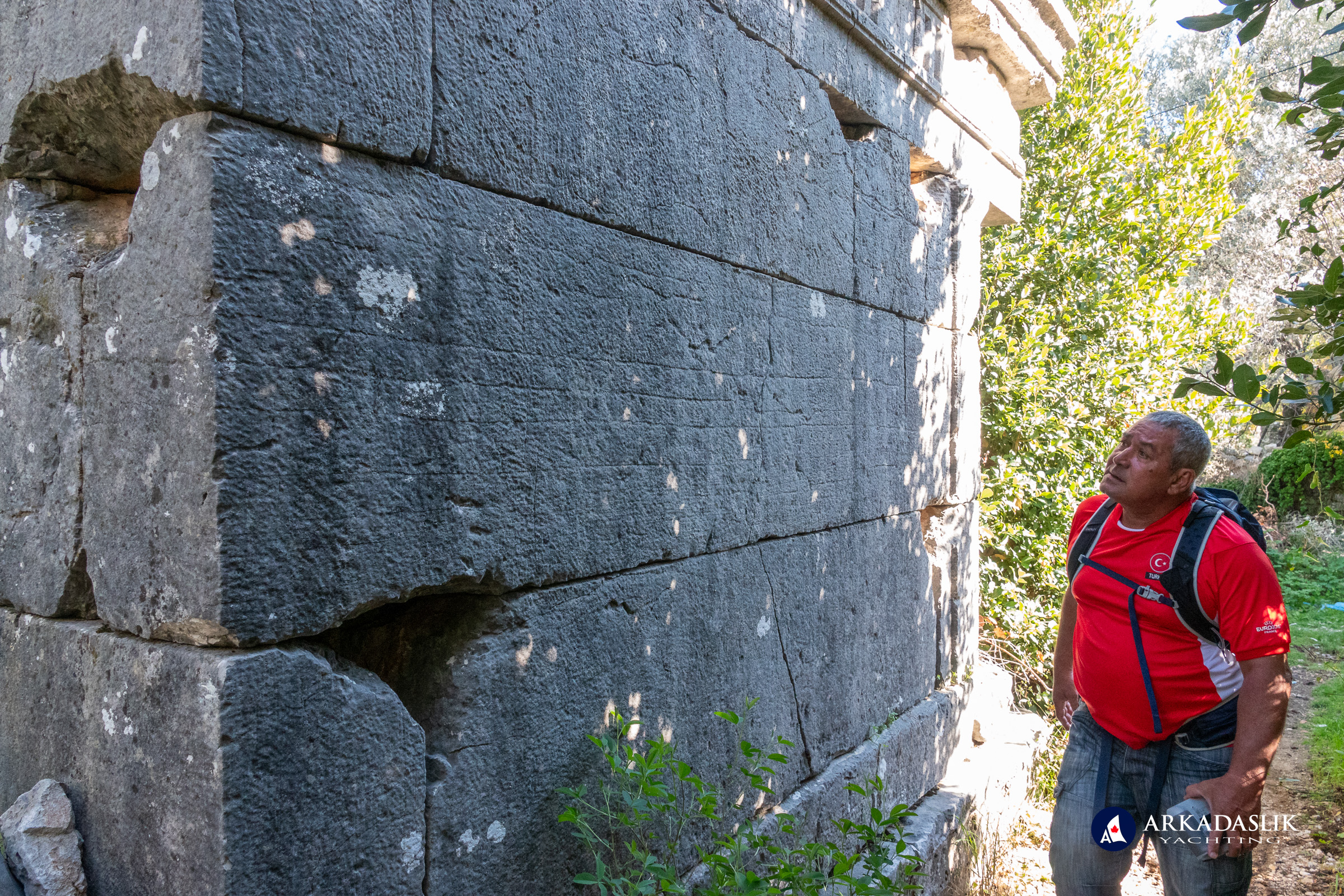 Visitor examining decorative carvings on an ancient structure at Sidyma